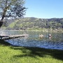Zwei Personen paddeln auf einem See neben einem Steg, umgeben von Hügeln und Bäumen.