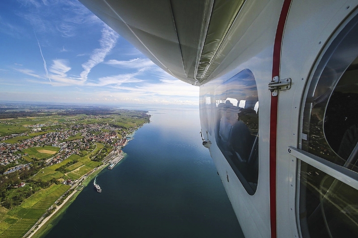 Blick aus einem Zeppelin über eine Landschaft und einen See bei klarem Himmel.