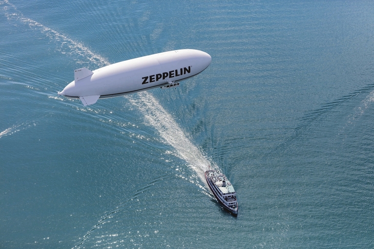 Zeppelin fliegt über Luftschiff und Boot auf offenem Wasser.