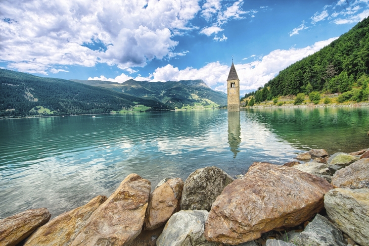 Glockenturm im Reschensee in Südtirol, Berge und Wolken im Hintergrund.