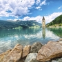 Glockenturm im Reschensee in Südtirol, Berge und Wolken im Hintergrund.
