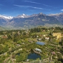 Luftaufnahme von Schloss Trauttmansdorff in Meran, umgeben von Gärten und Bergen.