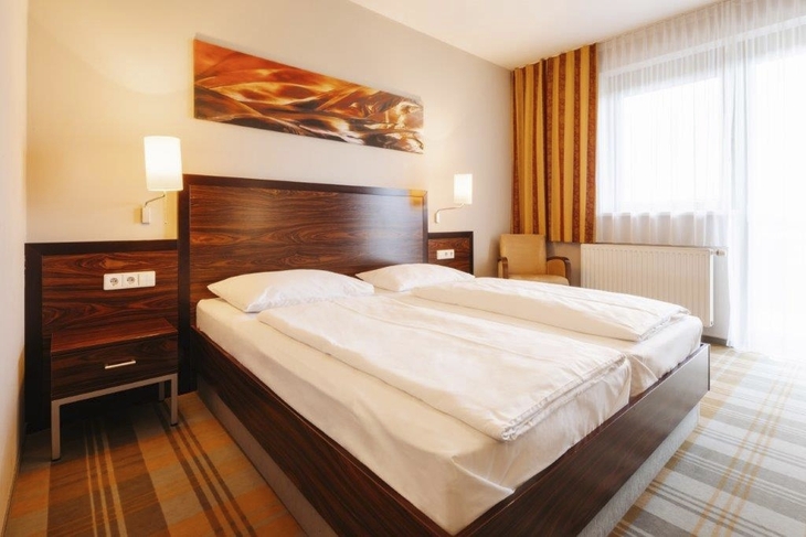 Hotelzimmer mit Doppelbett in modernem Design, helle Farben und großem Fenster.