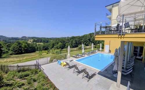 Hotelpool mit Liegestühlen und Blick auf grüne Landschaft bei Laßnitzhöhe.