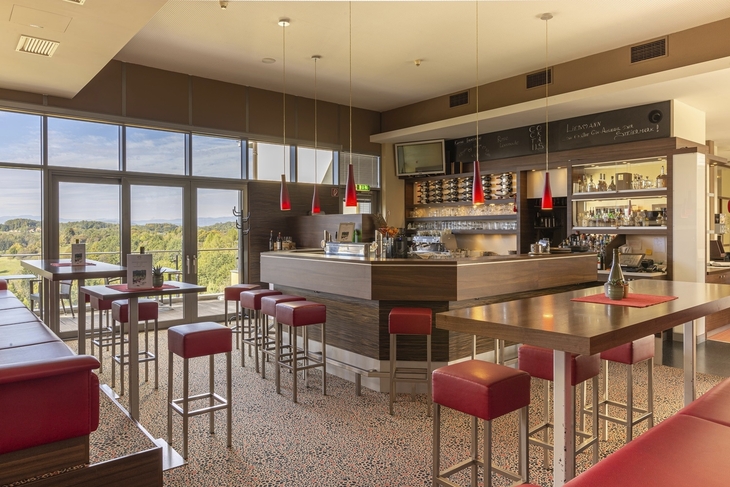 Moderne Hotelbar mit roten Barhockern und großer Fensterfront.