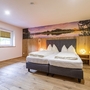 Schlafzimmer mit Doppelbett, Holzboden und großem Wandbild in warmen Farben.