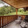 Überdachte Terrasse mit Holzgeländer und Gartenmöbeln vor bewaldeter Landschaft.