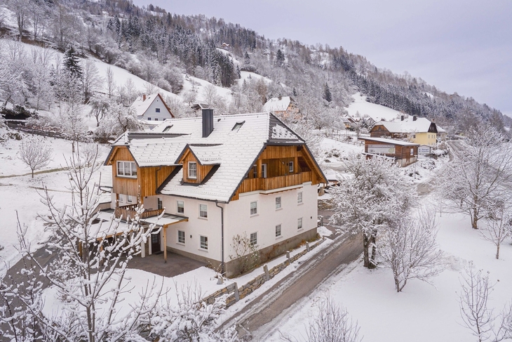 Winterliches Berghotel mit verschneiten Bäumen und Hügeln im Hintergrund.