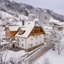 Winterliches Berghotel mit verschneiten Bäumen und Hügeln im Hintergrund.
