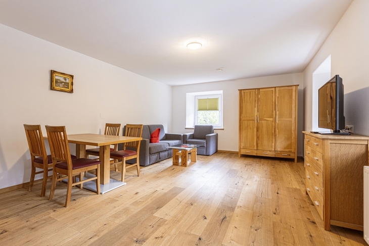 Wohnzimmer mit Essbereich, Holzboden, Schrank, Sofa und Fernseher.