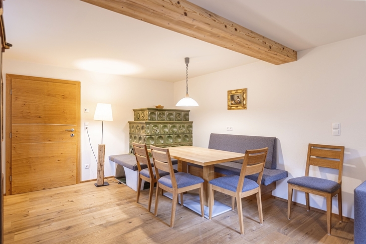 Essbereich mit Holztisch und Stühlen in gemütlicher Hütte, Wandlampe und grüner Ofen.