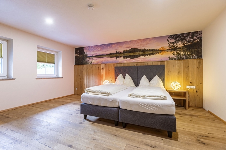 Schlafzimmer mit Doppelbett, Holzboden und großem Wandbild in warmen Farben.