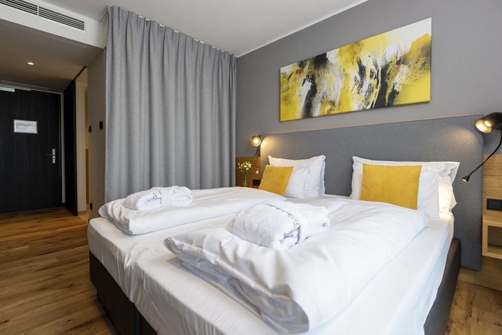 Modernes Hotelzimmer mit zwei Betten, gelben Kissen und abstraktem Kunstwerk.