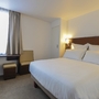 Helles Hotelzimmer mit großem Bett, Nachttischlampen und einem Fenster.