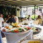 Gartenrestaurant mit gedeckten Tischen und serviertem Salat im Vordergrund.