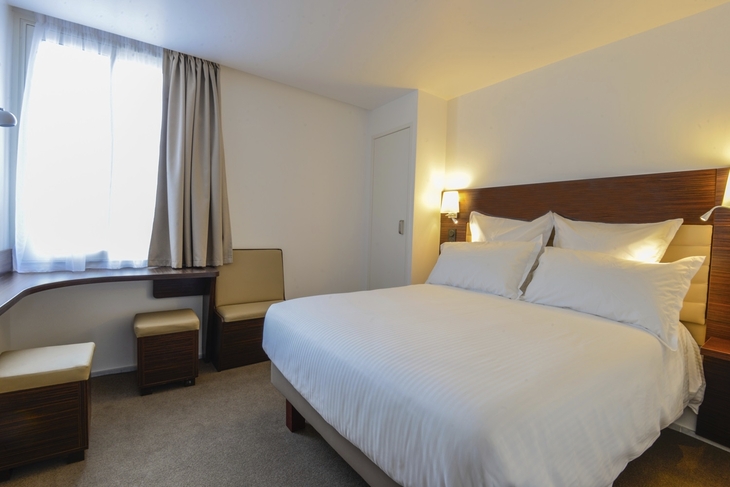 Helles Hotelzimmer mit großem Bett, Nachttischlampen und einem Fenster.