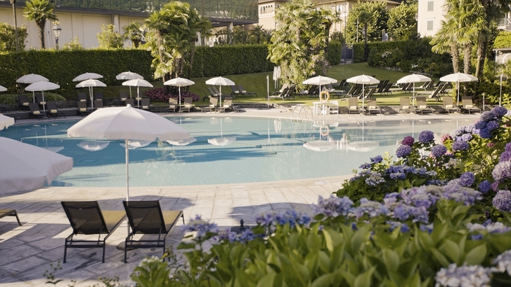Außenpool des Hotels Regina Palace mit Sonnenliegen und Sonnenschirmen im Garten.