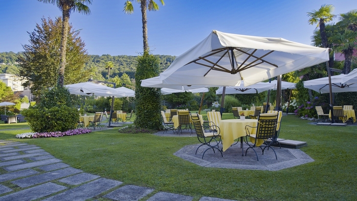 Garten des Hotels Regina Palace in Stresa mit Tischen, Stühlen und Sonnenschirmen
