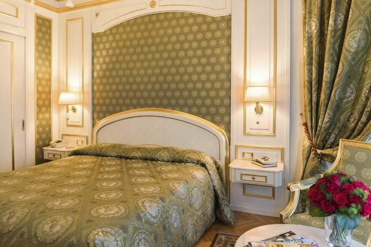 Elegantes Hotelzimmer mit grün-goldener Einrichtung und Blumenstrauß auf dem Tisch.