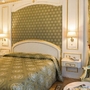 Elegantes Hotelzimmer mit grün-goldener Einrichtung und Blumenstrauß auf dem Tisch.
