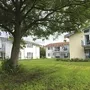 Drei Appartementhäuser an der Obstwiese, der Ferienanlage Lindau, mit Balkonen und Terrassen mit Outdoormöbeln ausgestattet und einem Baum auf einer grünen Wiese im Vordergrund.