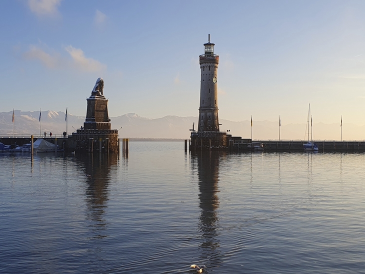 Hafeneinfahrt von Lindau mit Löwenstatue und Leuchtturm im Winter bei ruhigem Wasser