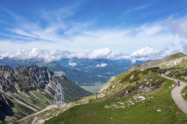 Aussicht auf Berglandschaft mit Seilbahn und Wanderweg bei Sonnenschein.
