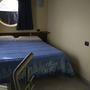 Hotelzimmer mit Bett, blauem Bettüberwurf und rundem Fenster.