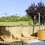 Außenbereich mit Holzliegen, Hecke und Baum vor Hügelkulisse.