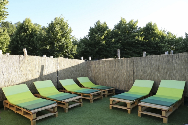 Holzlounge-Liegen im Freien vor einer Bambuswand und grünem Laub.
