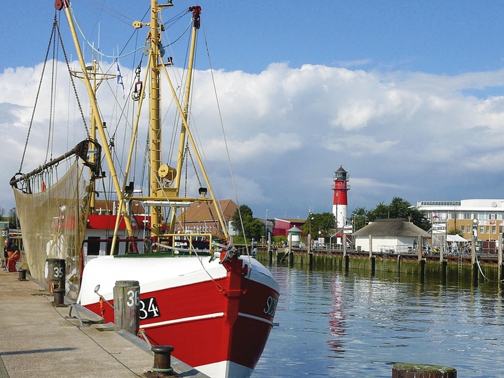 Fischkutter im Hafen von Büsum mit Leuchtturm im Hintergrund.