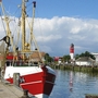 Fischkutter im Hafen von Büsum mit Leuchtturm im Hintergrund.