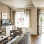 Wohnzimmer in Ferienwohnung mit Sofa, Sessel, Fernseher und großem Fenster zum Balkon.