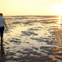 Person geht bei Sonnenuntergang im Watt der Nordsee.