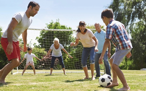 Familie spielt Fußball auf einem Rasenplatz bei sonnigem Wetter.