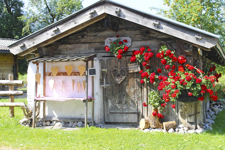Kleine Holzhütte mit Blumendekoration und Herzsymbolen, sonniger Tag.