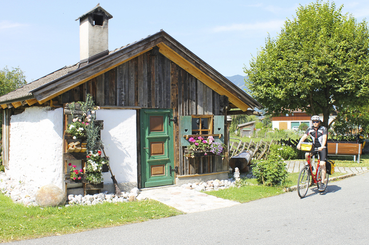 Radfahrer vor einem kleinen Holzhaus mit Blumen am Tauernradweg.