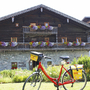 Rotes Fahrrad vor traditionellem Chalet mit blumengeschmücktem Balkon im Sommer.