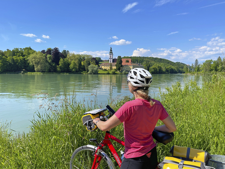 Radfahrerin genießt Ausblick am Tauernradweg entlang eines Flusses.