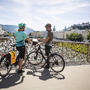 Zwei Radfahrer auf dem Makartsteg in Salzburg mit Blick auf die Stadt.