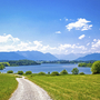 Radweg am Seeufer mit Alpen im Hintergrund und blauem Himmel.