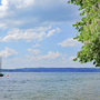 Blick auf den Starnberger See mit Boot, Bäumen und bewölktem Himmel.