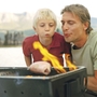Ein Mann und ein Kind pusten auf einem Grill ins Feuer.