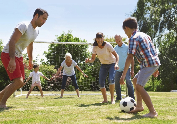 Familie spielt Fußball auf einem Rasenplatz bei sonnigem Wetter.