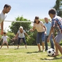 Familie spielt Fußball auf einem Rasenplatz bei sonnigem Wetter.