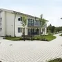 Modernes zweistöckiges Gebäude mit gepflastertem Weg und Bänken in einer Grünanlage.