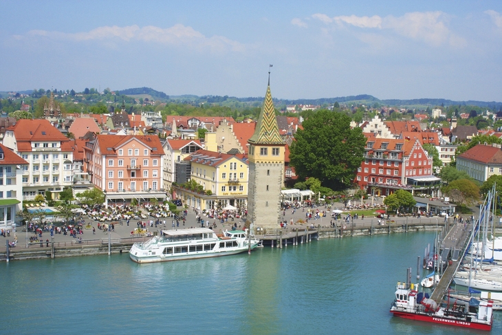 Blick auf Lindau am Bodensee mit Hafen, Booten und historischen Gebäuden unter leicht bewölktem Himmel.