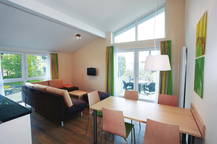 Helles Wohnzimmer mit Essbereich, Sofas, Tisch, großen Fenstern, modernen Möbeln.