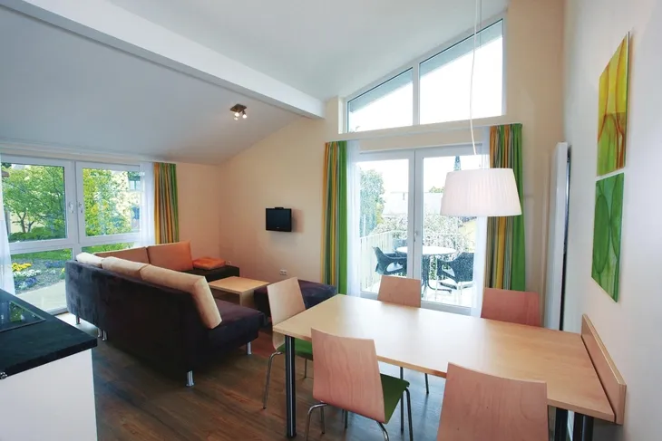 Helles Wohnzimmer mit Essbereich, Sofas, Tisch, großen Fenstern, modernen Möbeln.