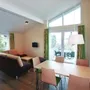 Helles Wohnzimmer mit Essbereich, Sofas, Tisch, großen Fenstern, modernen Möbeln.